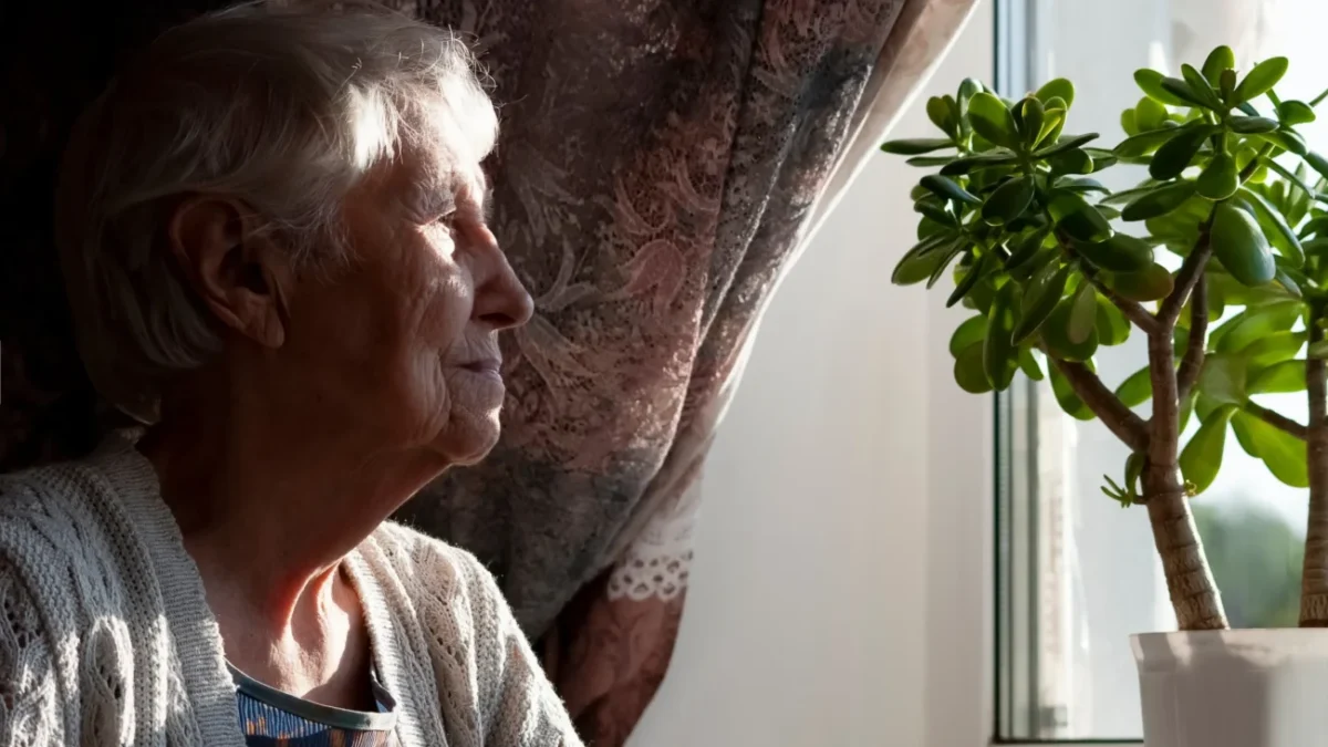 Osamocená seniorka dívající se z okna.