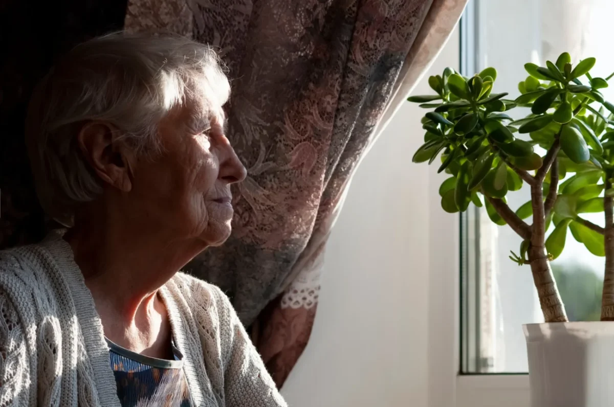 Osamocená seniorka dívající se z okna.