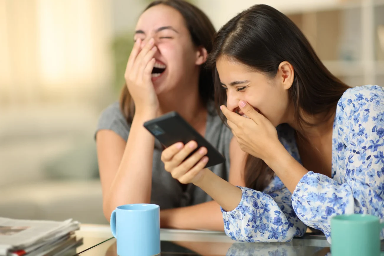 Dvě dívky se smějí na telefon.