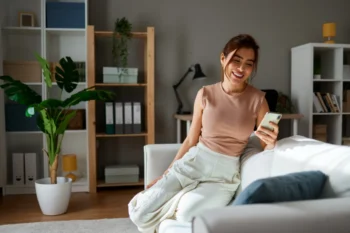 Žena sedí na gauči a směje se do telefonu.