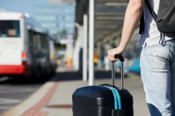 Muž stojí u autobusové zastávky s kufrem.
