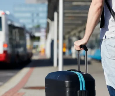 Muž stojí u autobusové zastávky s kufrem.