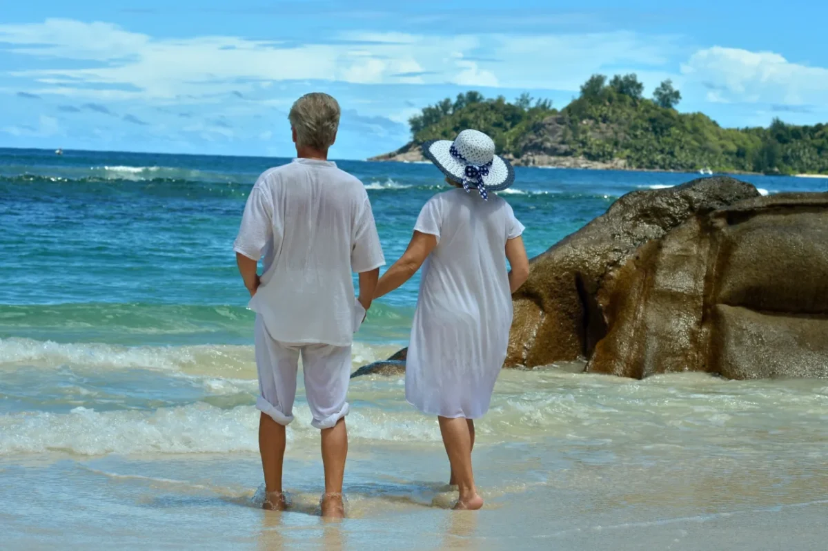 Babička s dědou se drží za ruku a dívají se do moře.