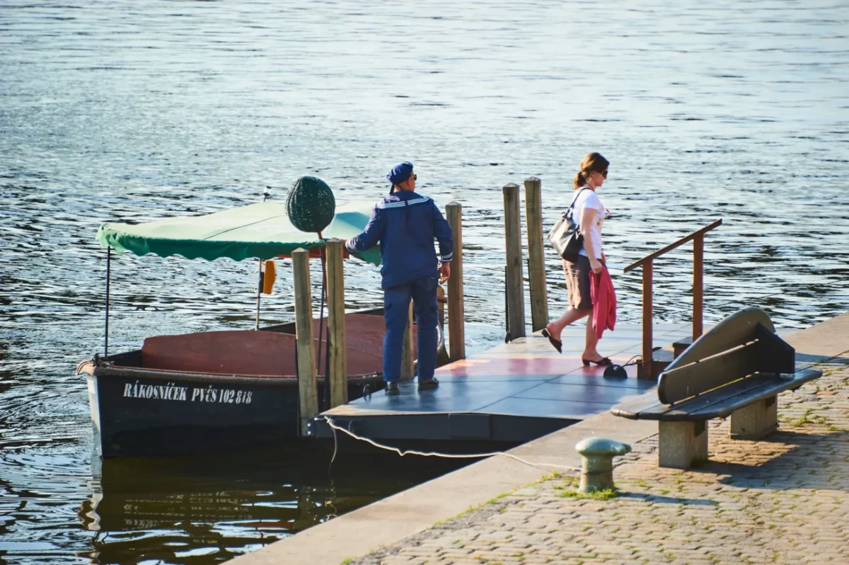 Žena vylezla z loďky, u které stojí kapitán.