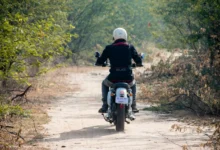 Muž jedoucí na motorce lesní cestou.