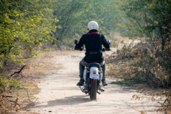 Muž jedoucí na motorce lesní cestou.