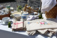 Na stole leží staré nádobí, ubrusy a utěrky.