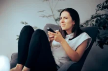 Žena sedí na křesle a nechápavě se dívá na televizi.