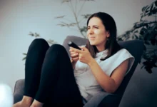 Žena sedí na křesle a nechápavě se dívá na televizi.