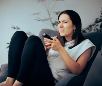 Žena sedí na křesle a nechápavě se dívá na televizi.