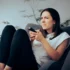 Žena sedí na křesle a nechápavě se dívá na televizi.