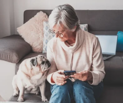 Seniorka sedí vedle svého psa u gauče.