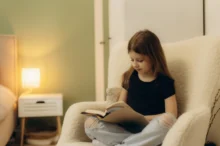 Holčička sedí v křesle a čte si.