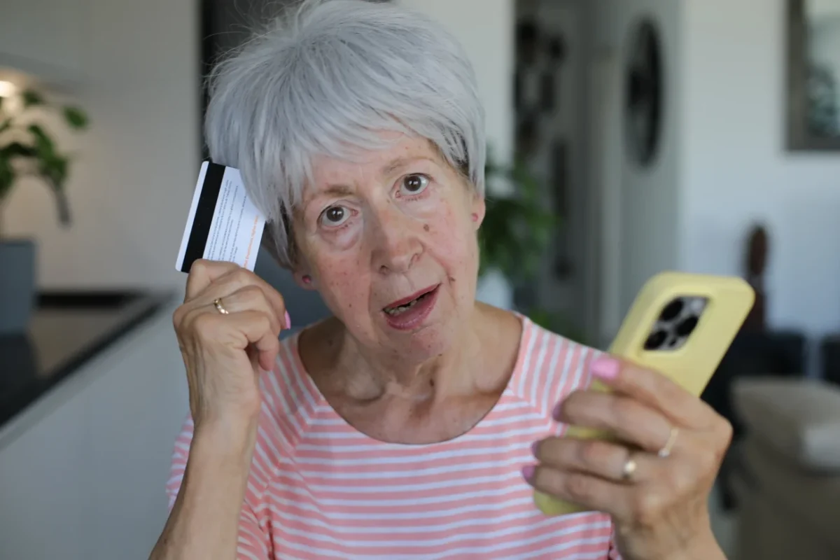 Starší žena v ruce drží telefon a platební kartu.