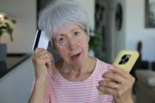 Starší žena v ruce drží telefon a platební kartu.