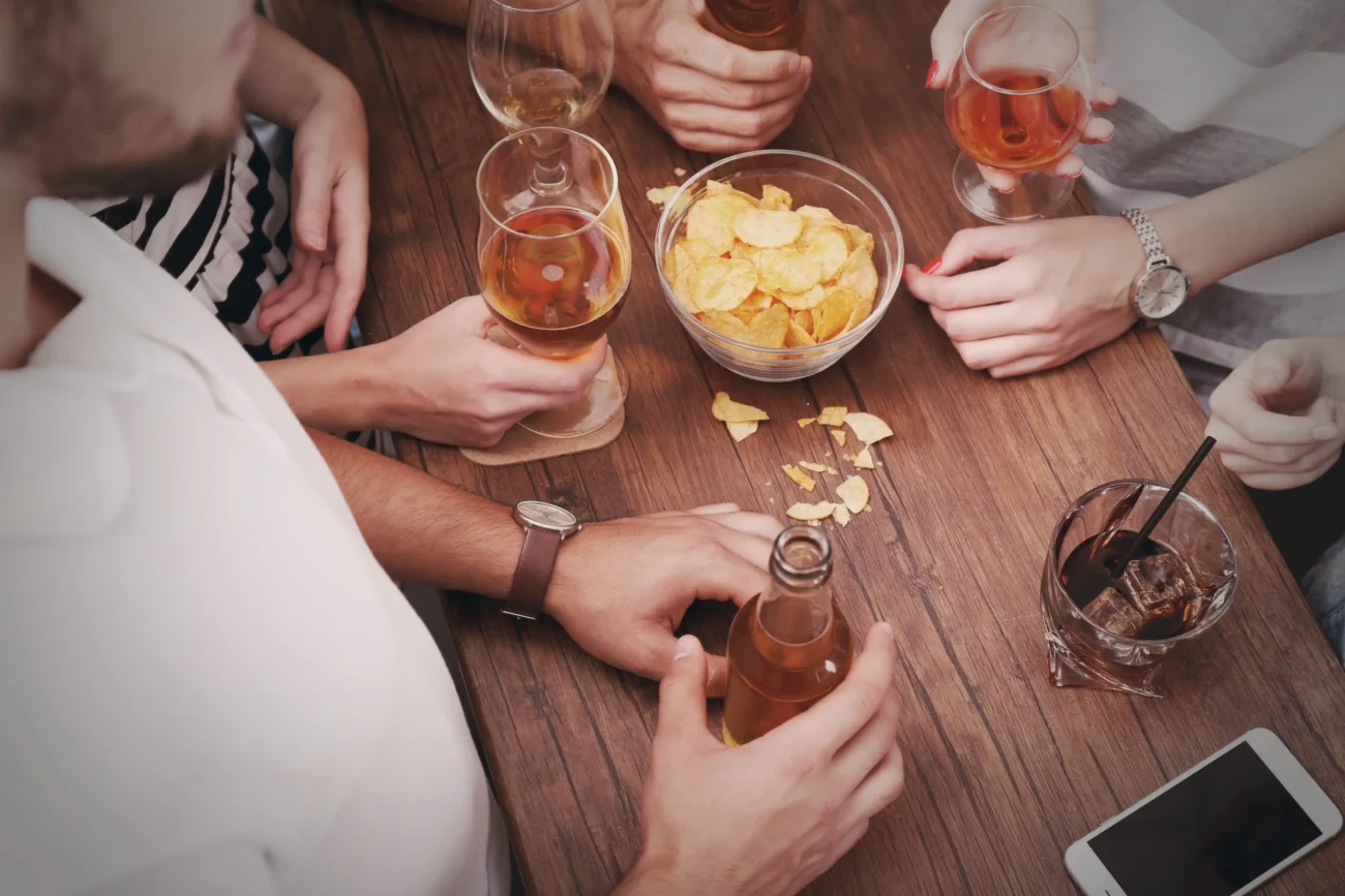 shutterstock_372712435-2 | TVGURU.cz Lidé sedí u stolu, na kterém jsou chipsy a alkohol.