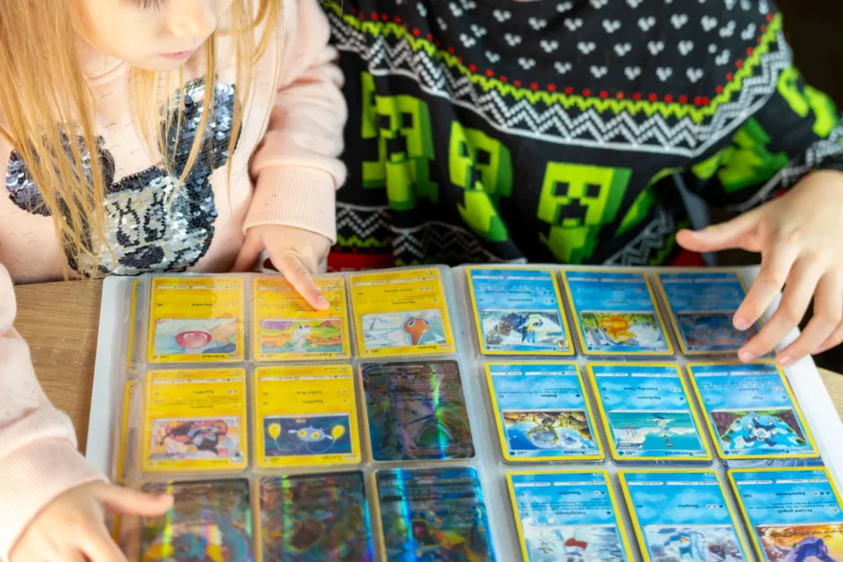 Dva školáci (dívka a chlapec) si společně prohlížejí album Pokémonů