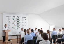 vědecká přednáška o DNA (viz informace na tabuli); profesor se skupinou studentů ve třídě