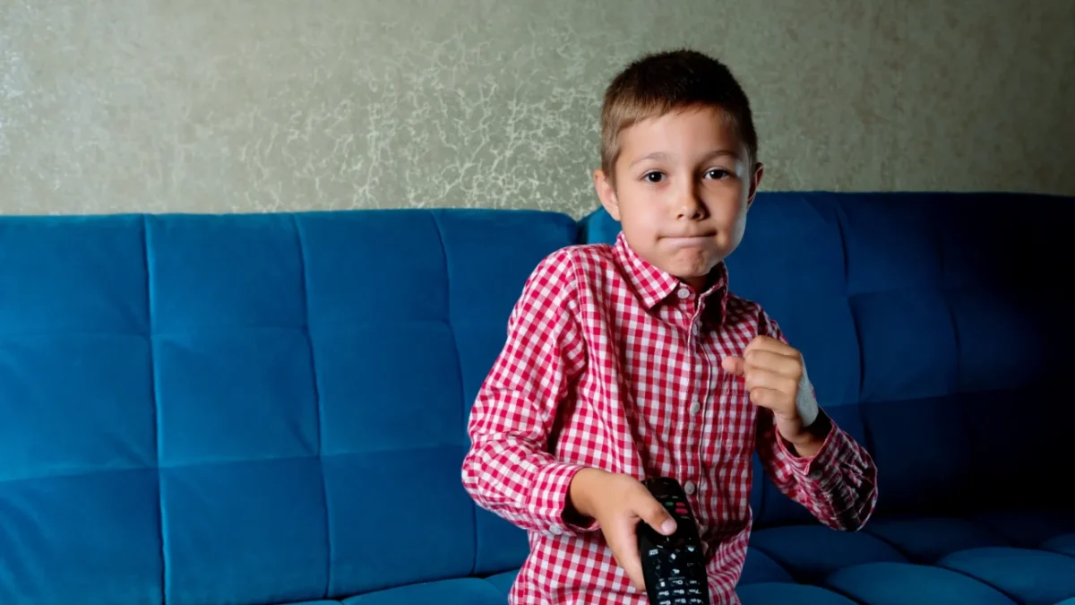 Chlapec sedí na gauči a v ruce drží ovladač od televize.