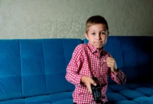 Chlapec sedí na gauči a v ruce drží ovladač od televize.
