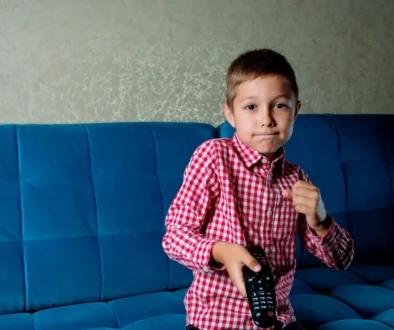 Chlapec sedí na gauči a v ruce drží ovladač od televize.