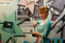 Lucille Ball ve voskovém muzeu Madame Tussaud v New Yorku - figurína se zrzavými vlasy v bleděmodrých šatech, s plakáty v pozadí.