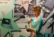 Lucille Ball ve voskovém muzeu Madame Tussaud v New Yorku - figurína se zrzavými vlasy v bleděmodrých šatech, s plakáty v pozadí.