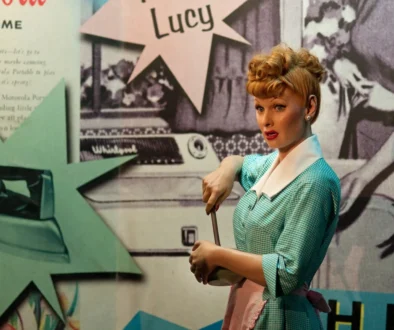 Lucille Ball ve voskovém muzeu Madame Tussaud v New Yorku - figurína se zrzavými vlasy v bleděmodrých šatech, s plakáty v pozadí.