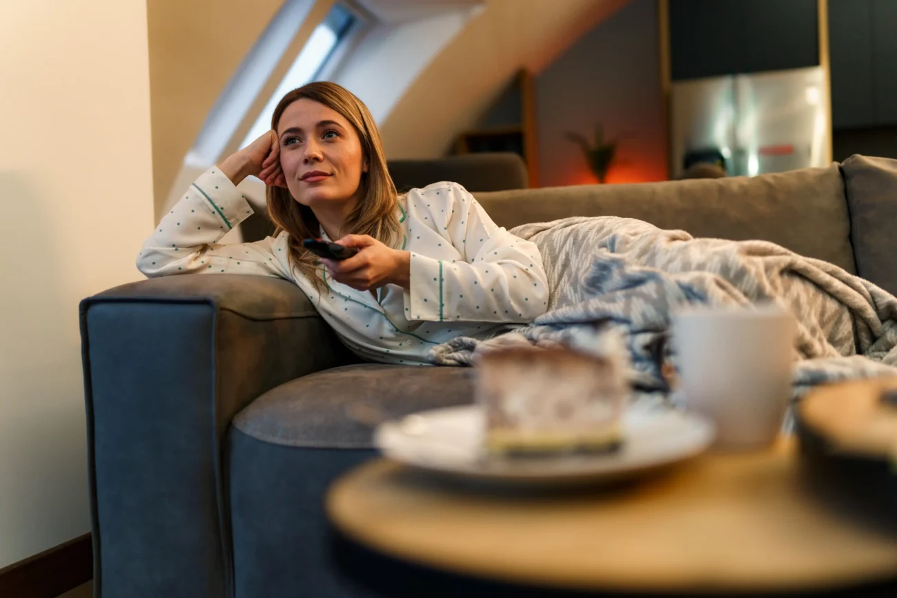 Česká televize uvede film, u kterého se rozhodně budete bavit. Zdroj: Shutterstock | TVGURU.cz Žena na gauči dívající se na televizi.