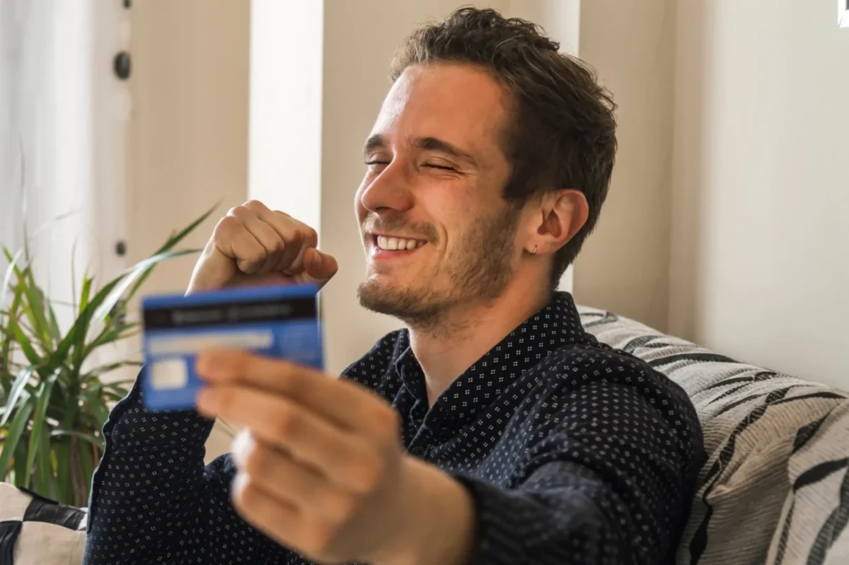 Muž se usmívá a drží v ruce platební kartu.