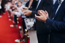 lidé stojí podél červeného koberce a tleskají