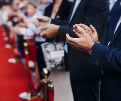 lidé stojí podél červeného koberce a tleskají