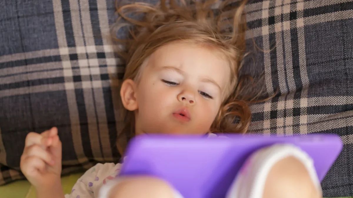 Holčička leží a dívá se na tablet.