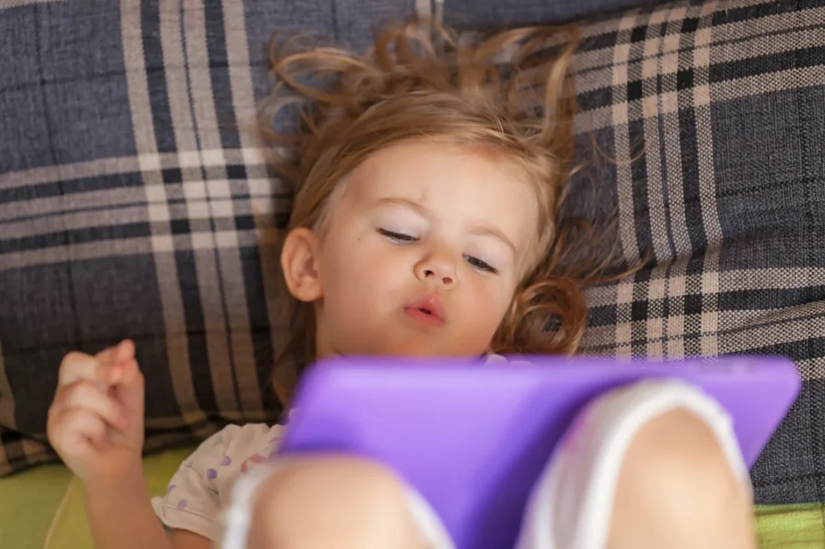 Holčička leží a dívá se na tablet.
