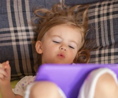Holčička leží a dívá se na tablet.