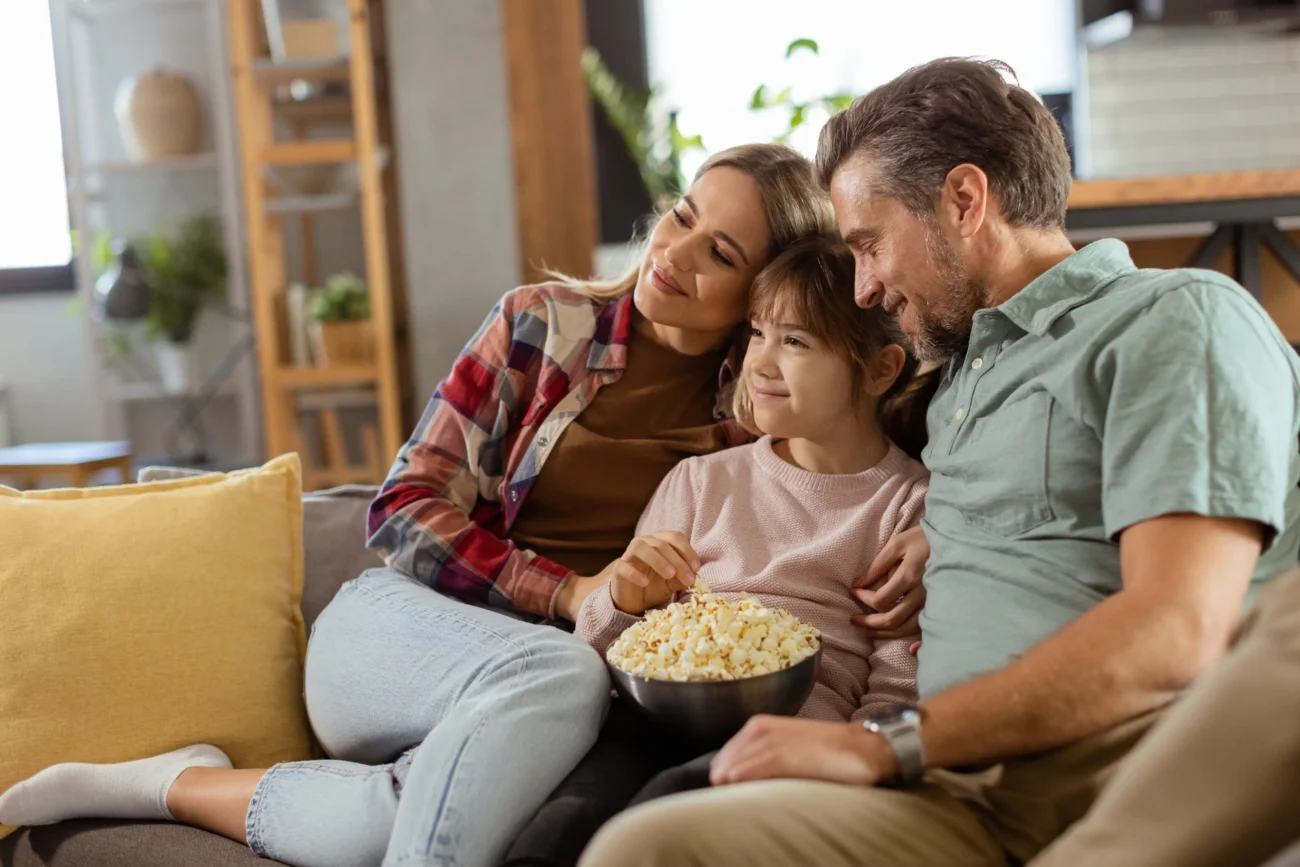 shutterstock_2432099849 1 | TVGURU.cz Rodina sedí na gauči s popcornem a kouká na televizi.