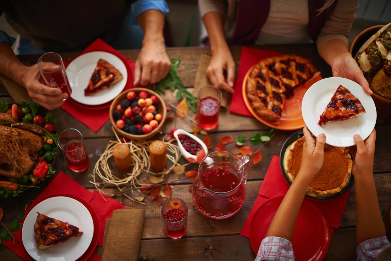 shutterstock_3071562261 | TVGURU.cz Detail stolu se zahradním menu (koláč, rybízový nápoj); několik rukou na stole, příjemná atmosféra