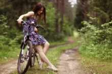 Žena je na lesní cestě opřená o kolo.