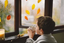 Malý kluk pije čaj a kouká, jak za oknem prší.