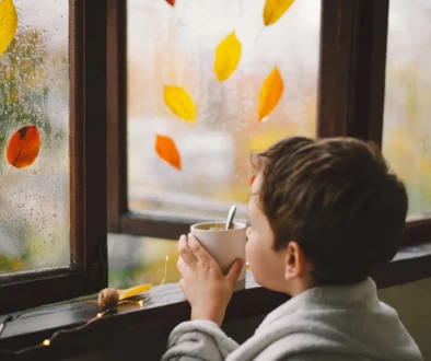 Malý kluk pije čaj a kouká, jak za oknem prší.