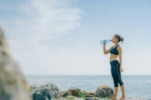 Žena stojí u moře a pije vodu.