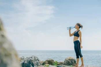 Žena stojí u moře a pije vodu.