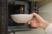 ruka drží misku a vkládá ji do mikrovlnné trouby