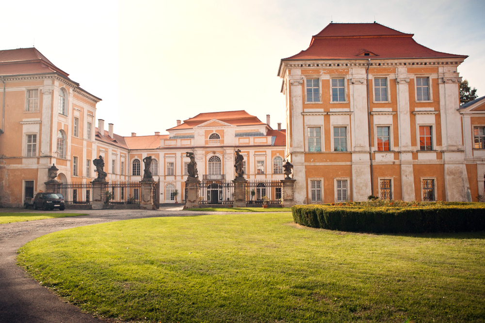 shutterstock_1278183637 | TVGURU.cz Zámek Duchcov zvenčí od příjezdové cesty za jasného dne, zelená tráva, jaro