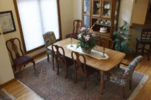 Starožitná vitrína, prosklená, dřevěná, v "hostinském pokoji" s velkým dřevěným stolem, kobercem a oknem.