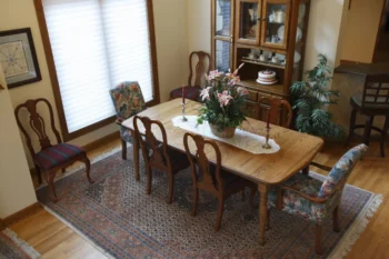 Starožitná vitrína, prosklená, dřevěná, v "hostinském pokoji" s velkým dřevěným stolem, kobercem a oknem.