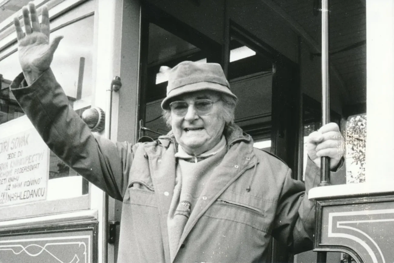 Jiří Sovák mává a vylézá z tramvaje.