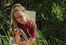 Žena sedí na zahradě a kouká se do telefonu.