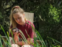 Žena sedí na zahradě a kouká se do telefonu.