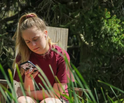 Žena sedí na zahradě a kouká se do telefonu.